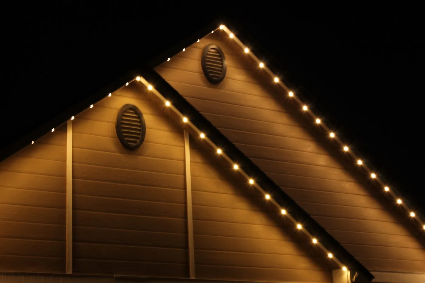 The same two gables at night, lit in warm white by the permanent roofline lighting